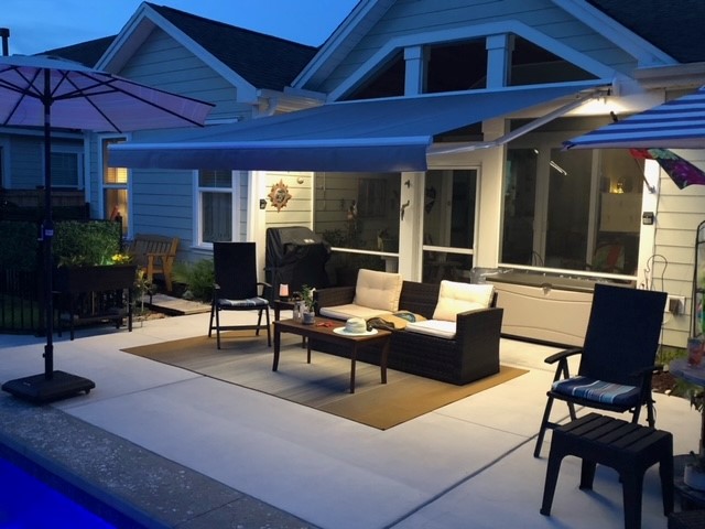 Motorized retractable awning with LED lighting illuminating a luxury outdoor living room with sofa and lounge chairs at dusk