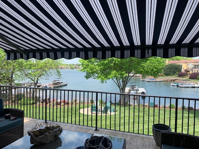 View from underneath a black and white striped retractable awning looking out over a lakefront with boats and waterfront homes